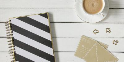 Flatlay of a striped notebook, coffee cup, and envelopes on a wooden desk.