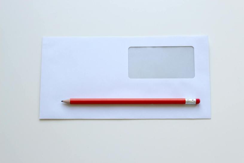 Minimalist photo of a red pencil on a blank white envelope with window. Perfect for stationery themes.