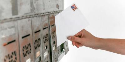 Close-up of a hand inserting a stamped envelope into a mailbox, symbolizing voting.